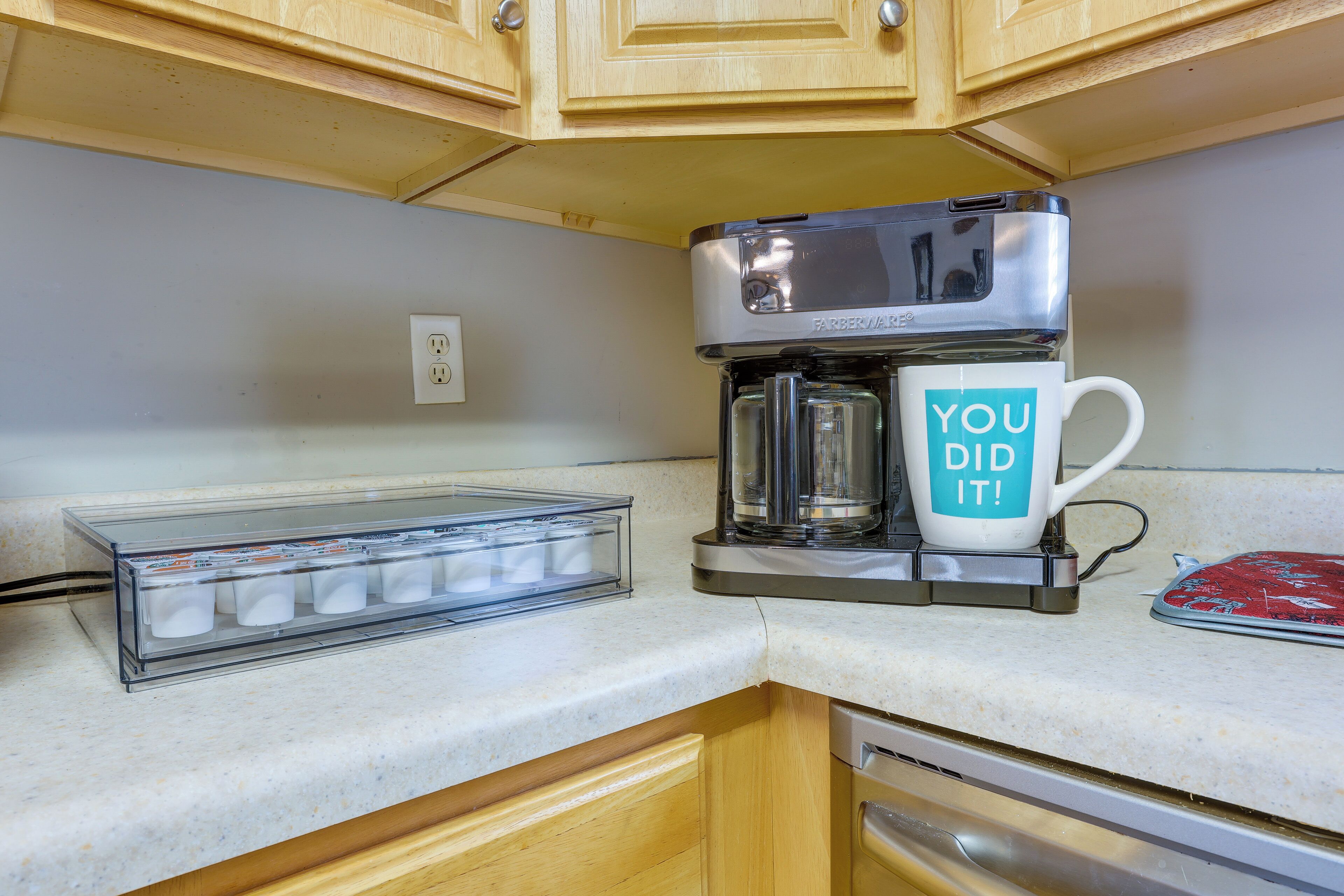A kitchen with a coffee maker, a mug with "YOU DID IT!" text, and a clear plastic container with items.