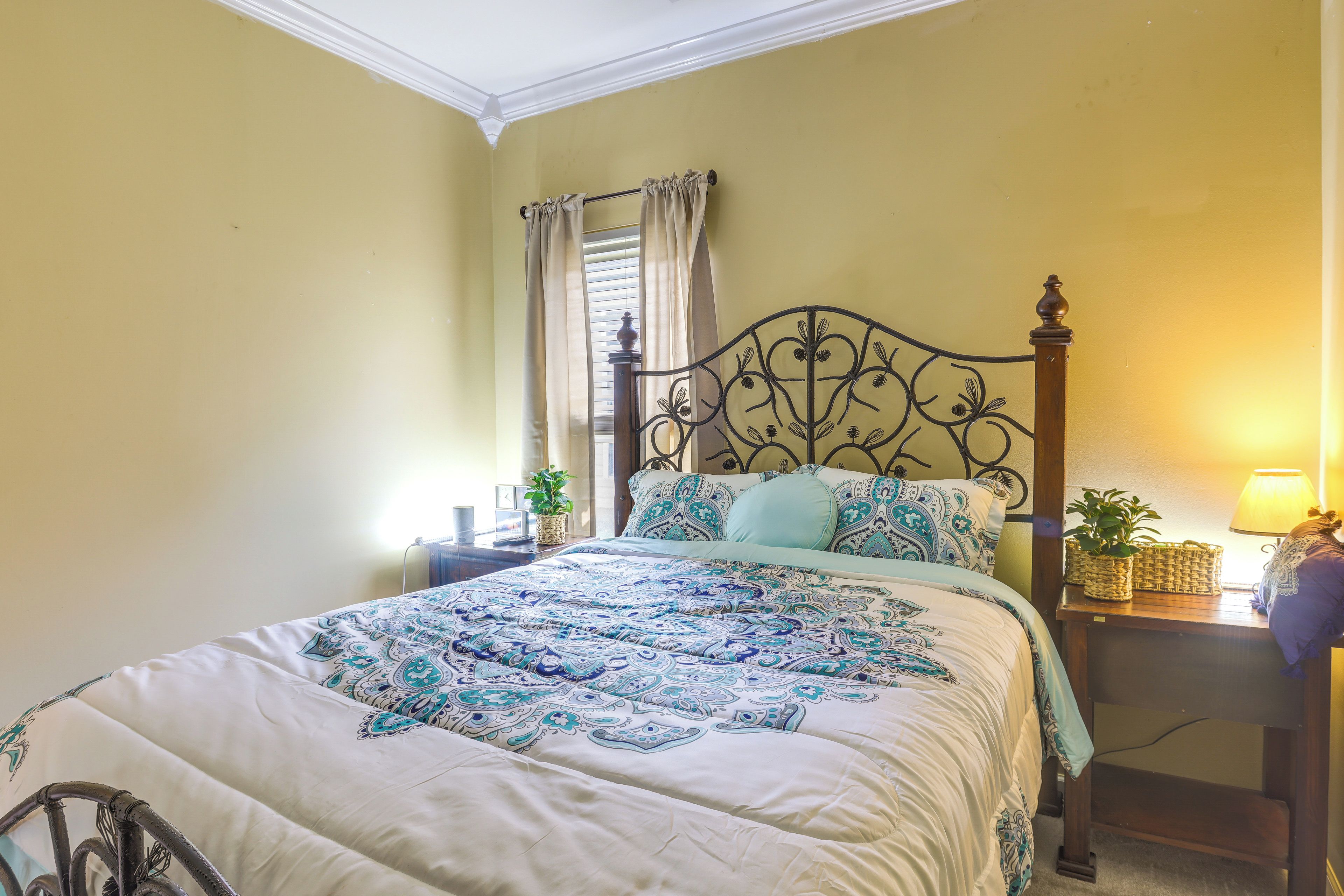 A bed with a patterned bedspread, a bedside table with a lamp, and a window with curtains.