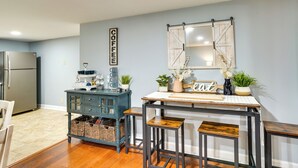 Une cuisine avec une table en bois, des tabourets de bar, un réfrigérateur et un miroir fixé au mur.