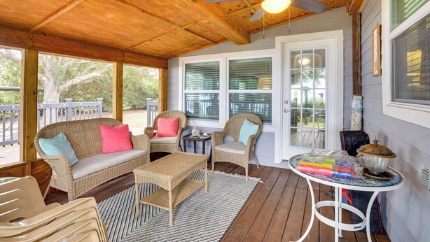 Une véranda couverte, meublée de meubles en osier, dotée d’un ventilateur de plafond et d’une table sur laquelle est posé un vase décoratif.