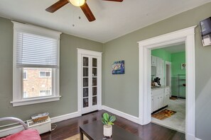 A room with a wooden ceiling fan, a window with blinds, a white door, a kitchen area with green walls, and a plant on a table. - Walk to Restaurants: Cozy, Convenient Jennings Apt (Jennings)