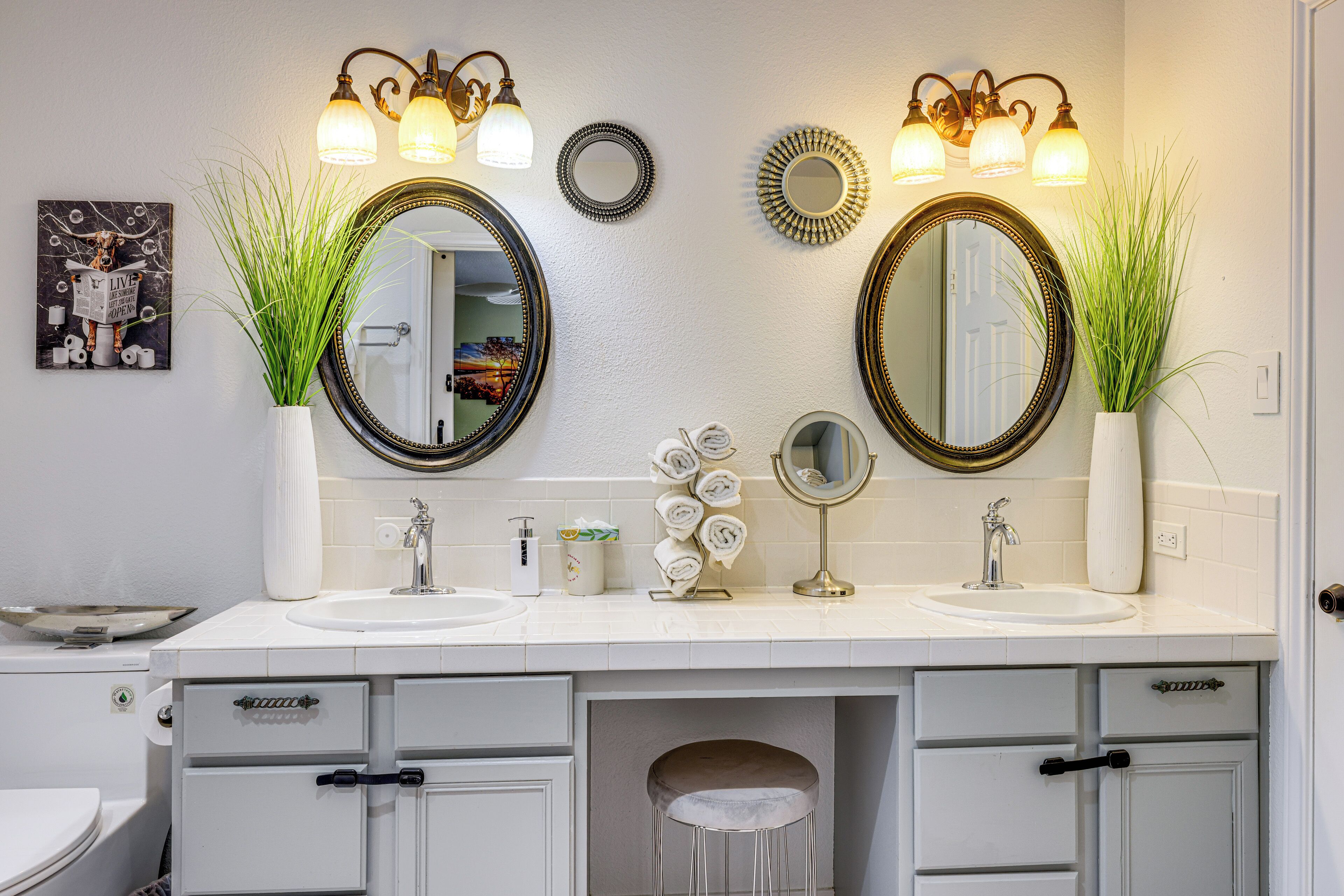 A bathroom with two sinks, a toilet, and a vanity with drawers. There are two mirrors above the sinks, each with a light fixture.