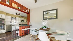 Une cuisine moderne avec des meubles blancs, un îlot central en bois et un coin repas comprenant une table en verre et des chaises blanches.