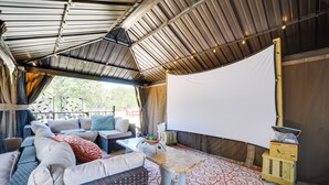 Un espace extérieur aménagé avec un canapé, une table et un grand écran blanc, probablement utilisé pour des projections de films en plein air ou des présentations.