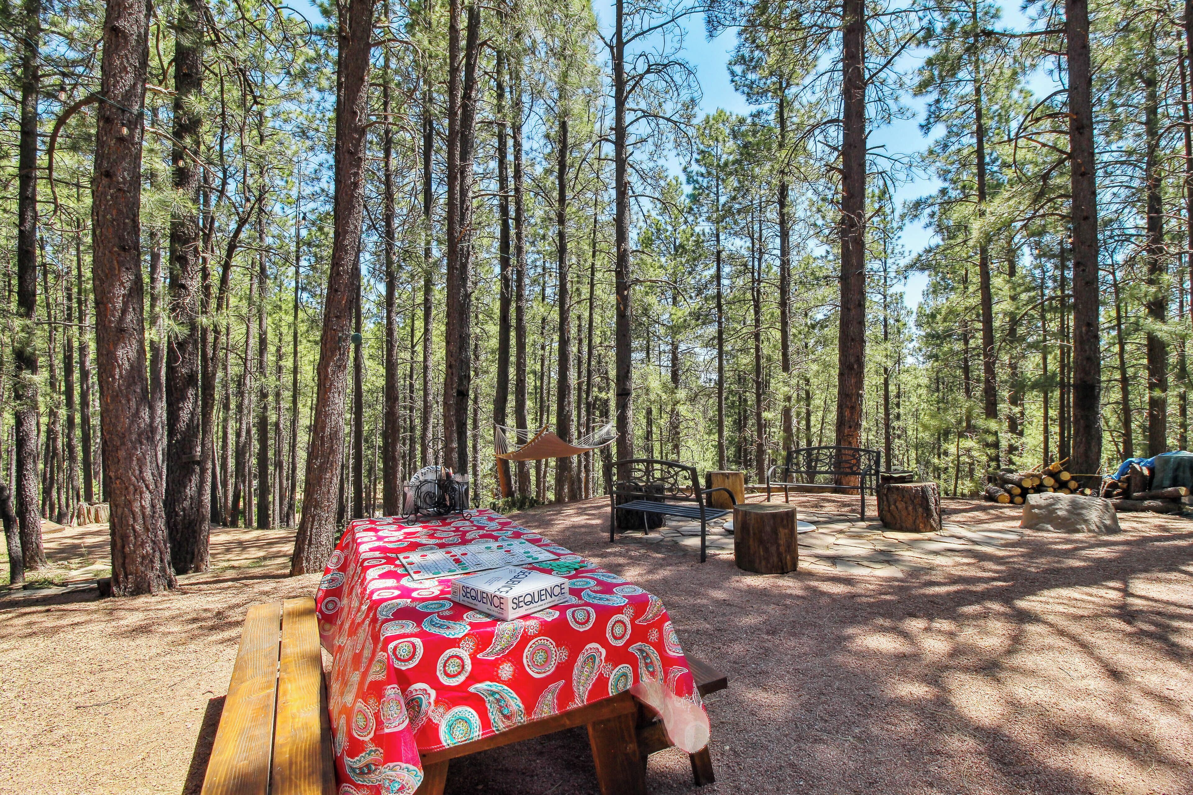 Cacifato en un bosque con una mesa de picnic cubierta por un mantel rojo estampado, rodeado de altos pinos.