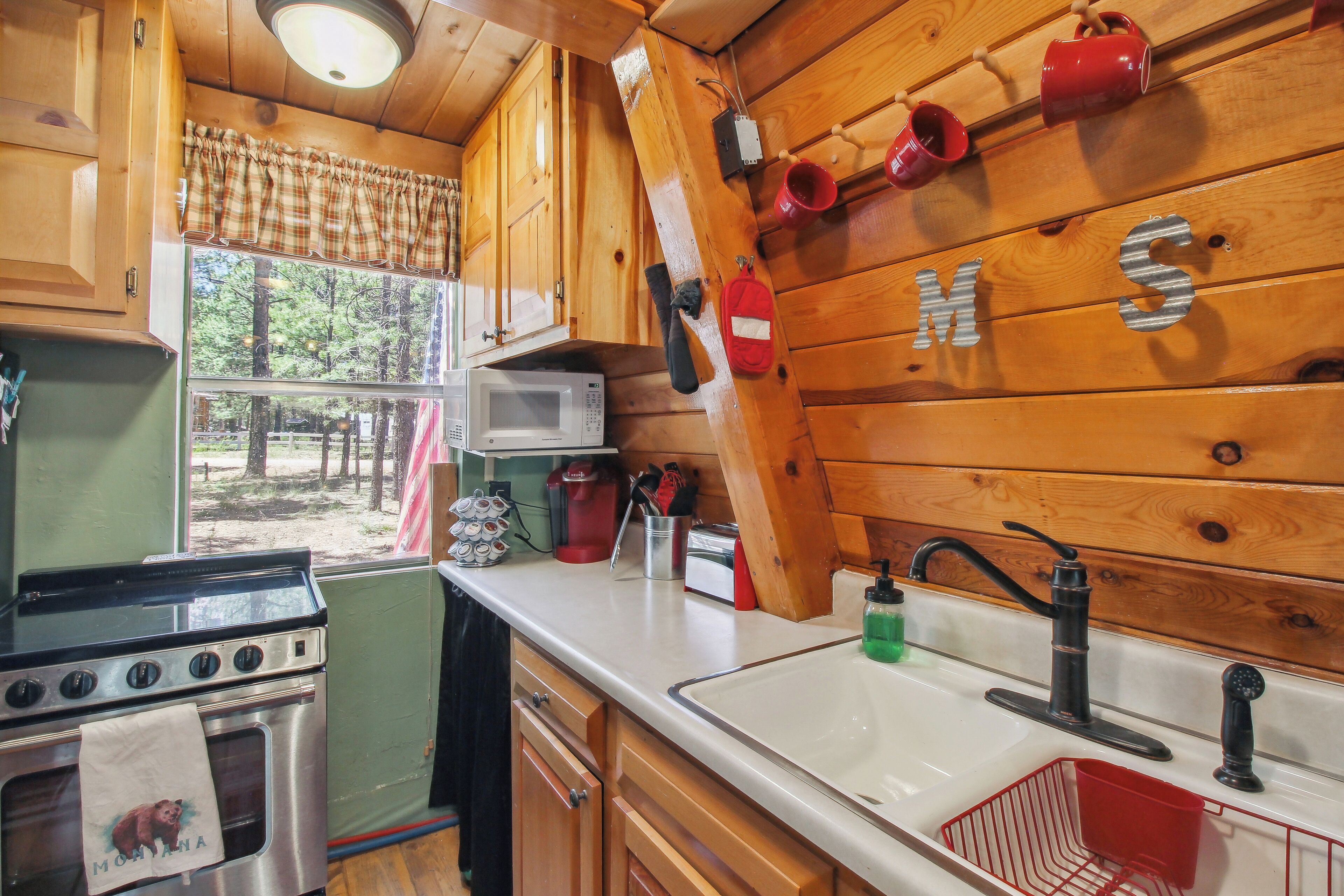 A rustic kitchen with wooden walls, a stove, a microwave, and a sink.