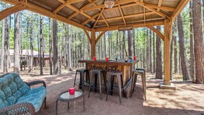 A covered outdoor seating area with a bar, stools, and a wicker sofa. - Near Trails: Forest Lake Retreat w/ Backyard Oasis (Forest Lakes)