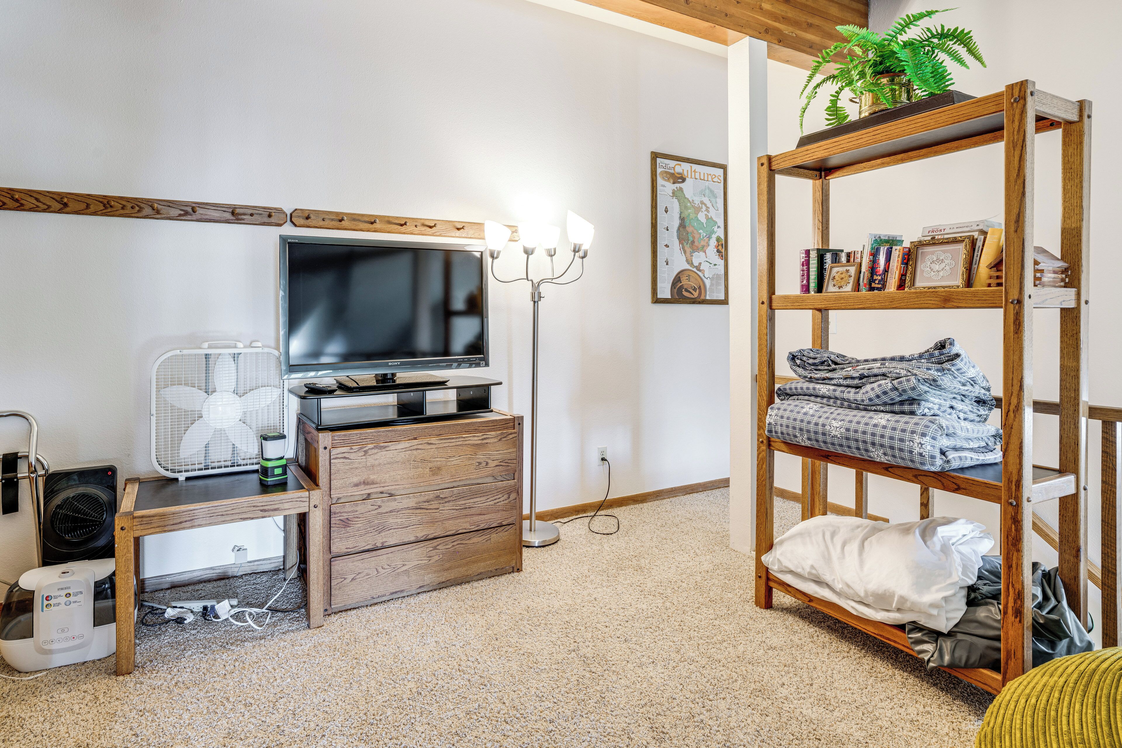 A room with a television, wooden furniture, a fan, a shelf with books, and a plant.