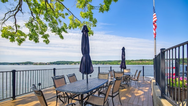 A deck with outdoor seating, a flag, and a view of a body of water. - Lake Ozark Vacation Rental w/ Pool Access (Lake Ozark)