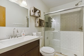 A bathroom with a white sink, a toilet, a glass-enclosed shower, and wicker baskets on the wall. - Lake Ozark Vacation Rental w/ Pool Access (Lake Ozark)
