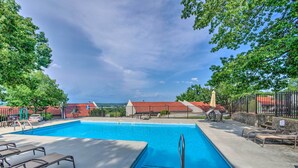 A swimming pool with lounge chairs, a lifeguard stand, and a view of buildings with red roofs.