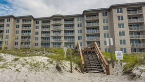 A multi-story building with balconies and a staircase leading to a sandy area. - Fort Walton Beach Rental w/ Pool & Hot Tub Access (Fort Walton Beach)