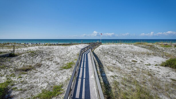 A beach path leading to the ocean with a wooden railing and a flag at the end.