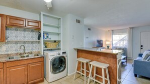 A compact kitchen with a washing machine, wooden cabinets, and a small bar area.