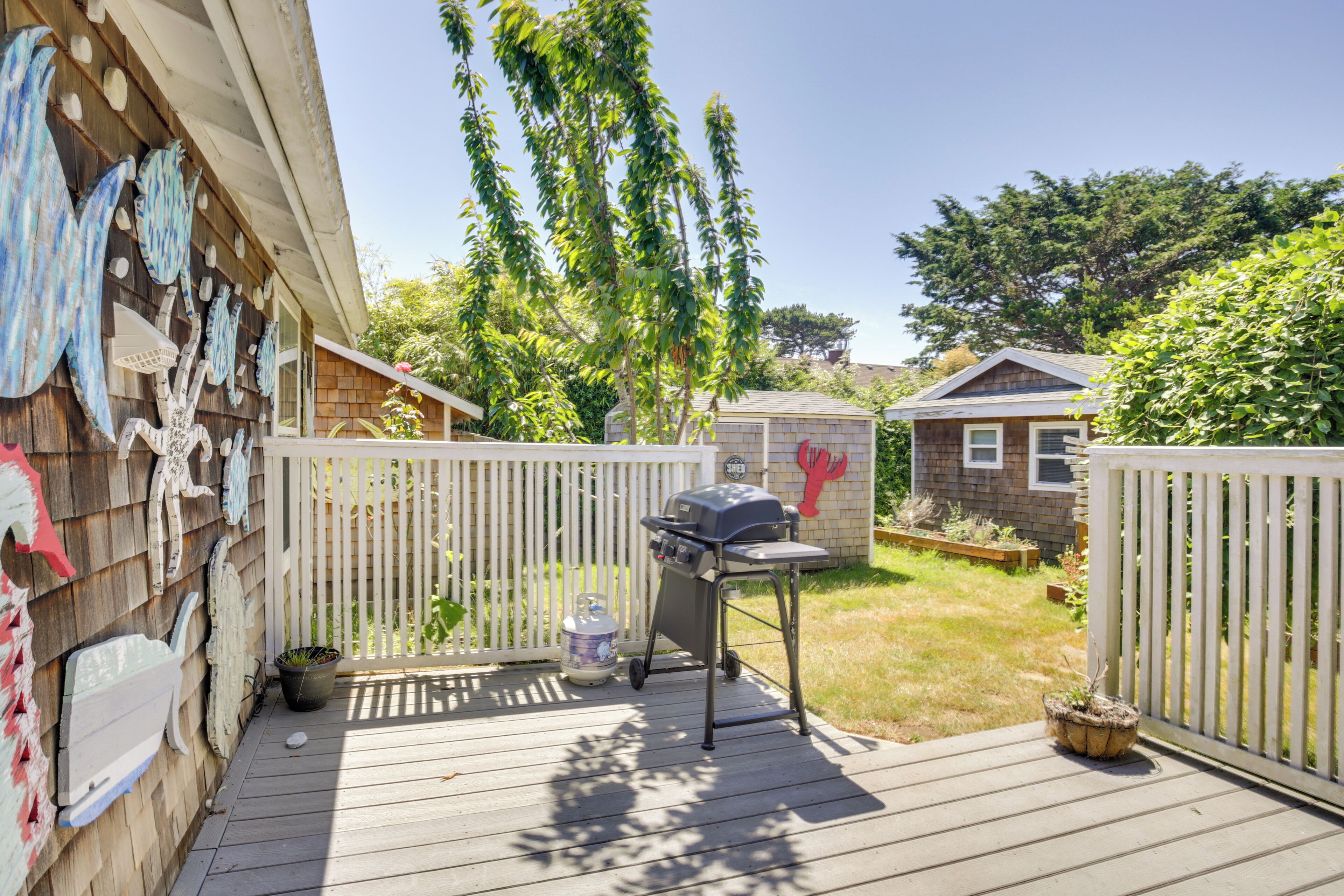 A wooden deck with a barbecue grill, a white fence, and a small shed.