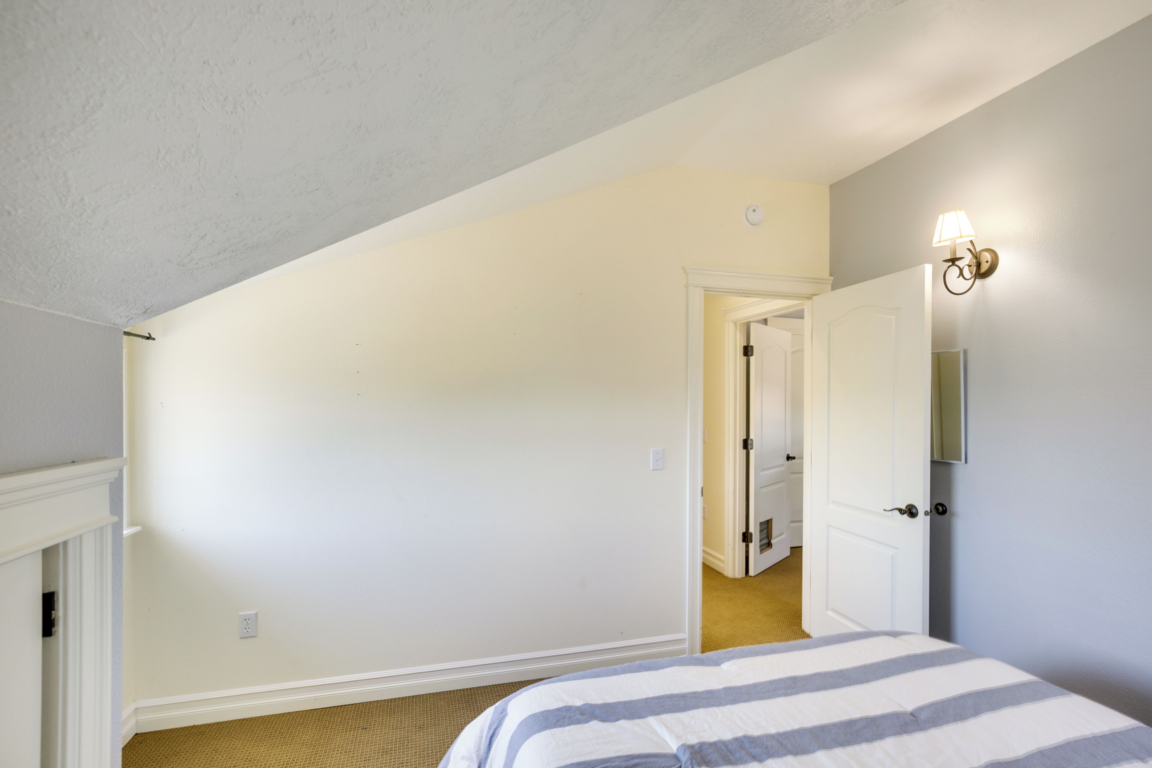 A bedroom with a bed, a door, and a light fixture on the wall.