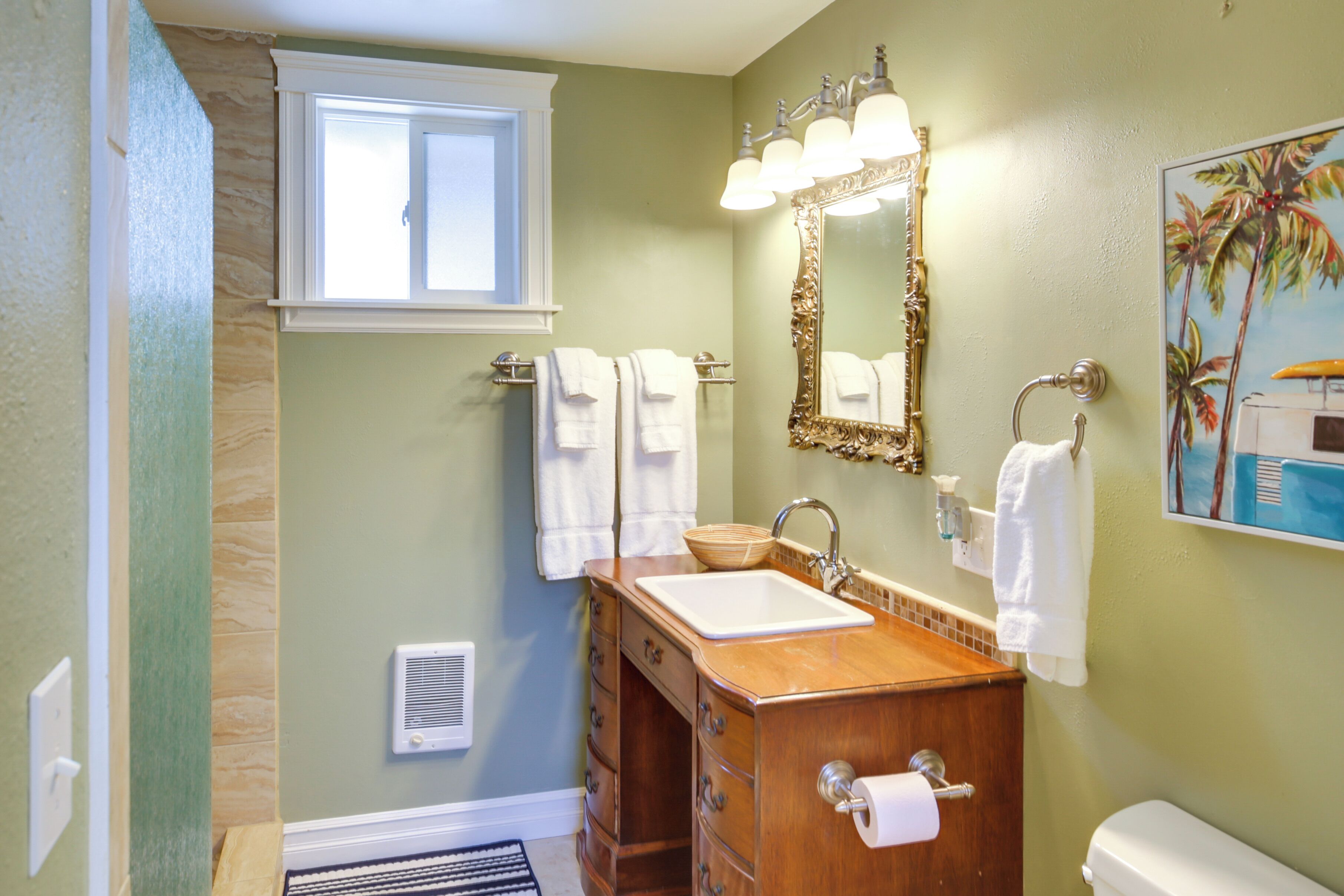 Un baño con tocador de madera, lavamanos blanco, espejo con luces y perchero para toallas.