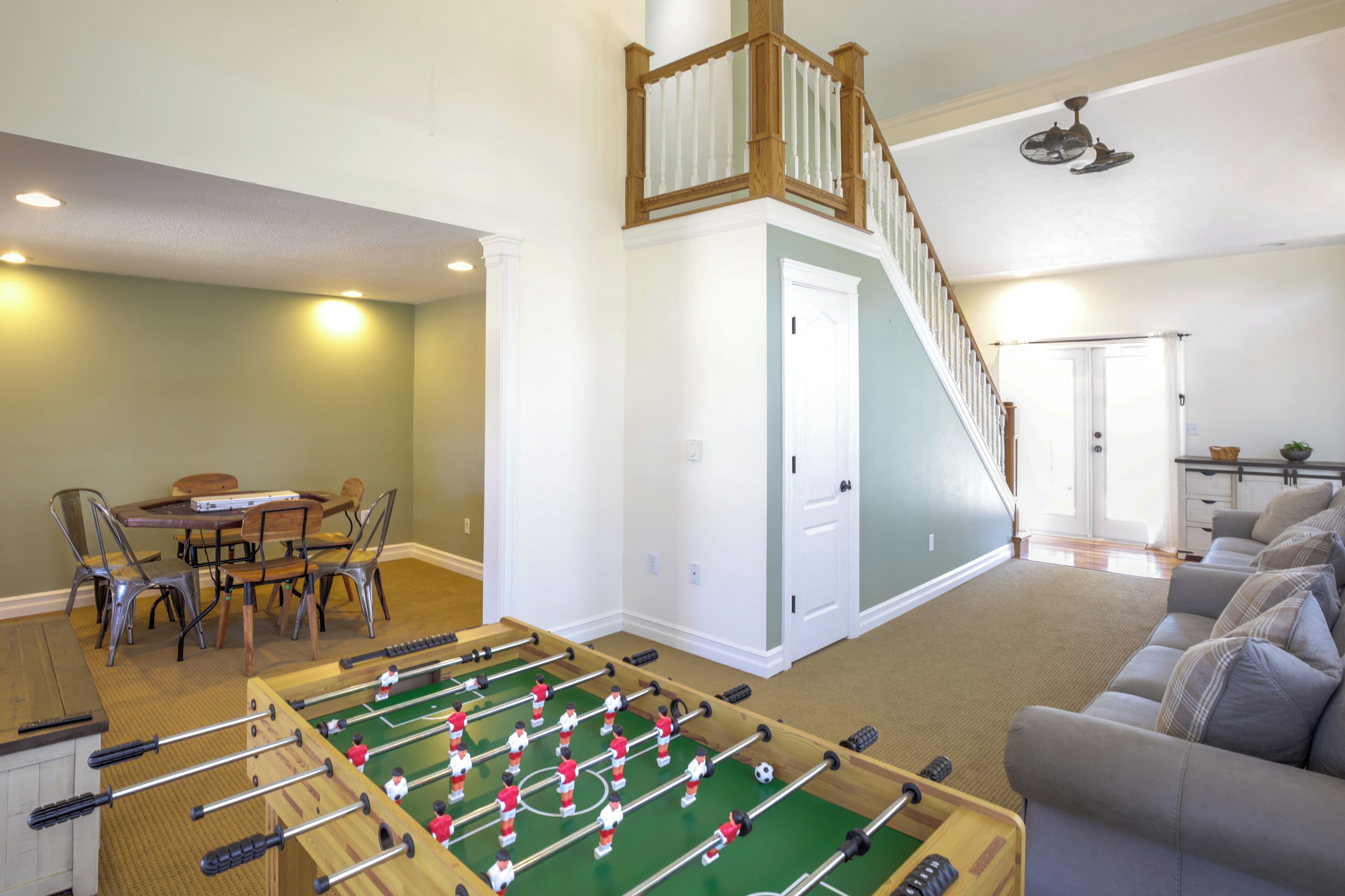 A living room with a foosball table, a staircase, and a dining area with chairs and a table.