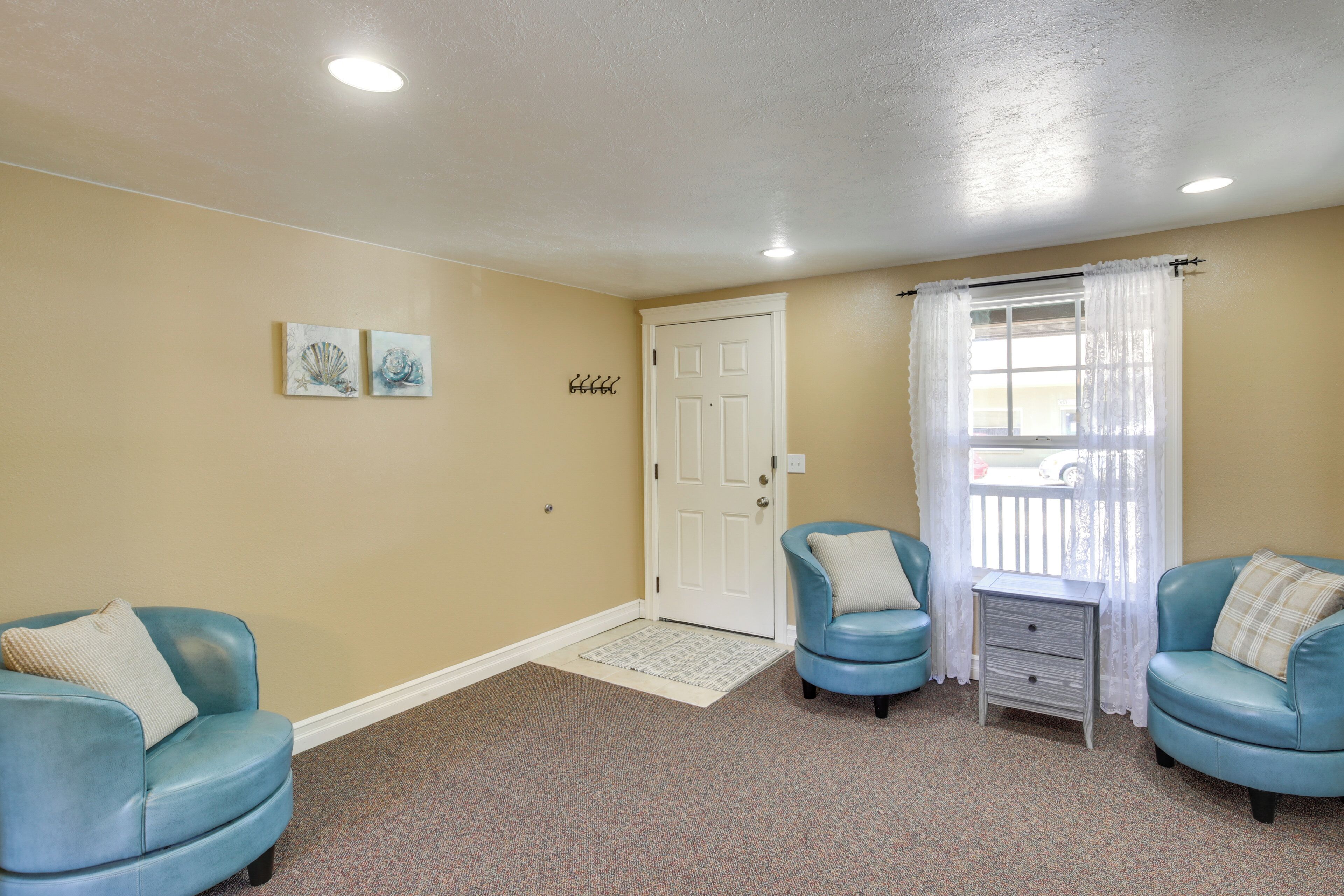 A room with two blue leather chairs, a white door, a small table with a drawer, and two wall-mounted hooks.