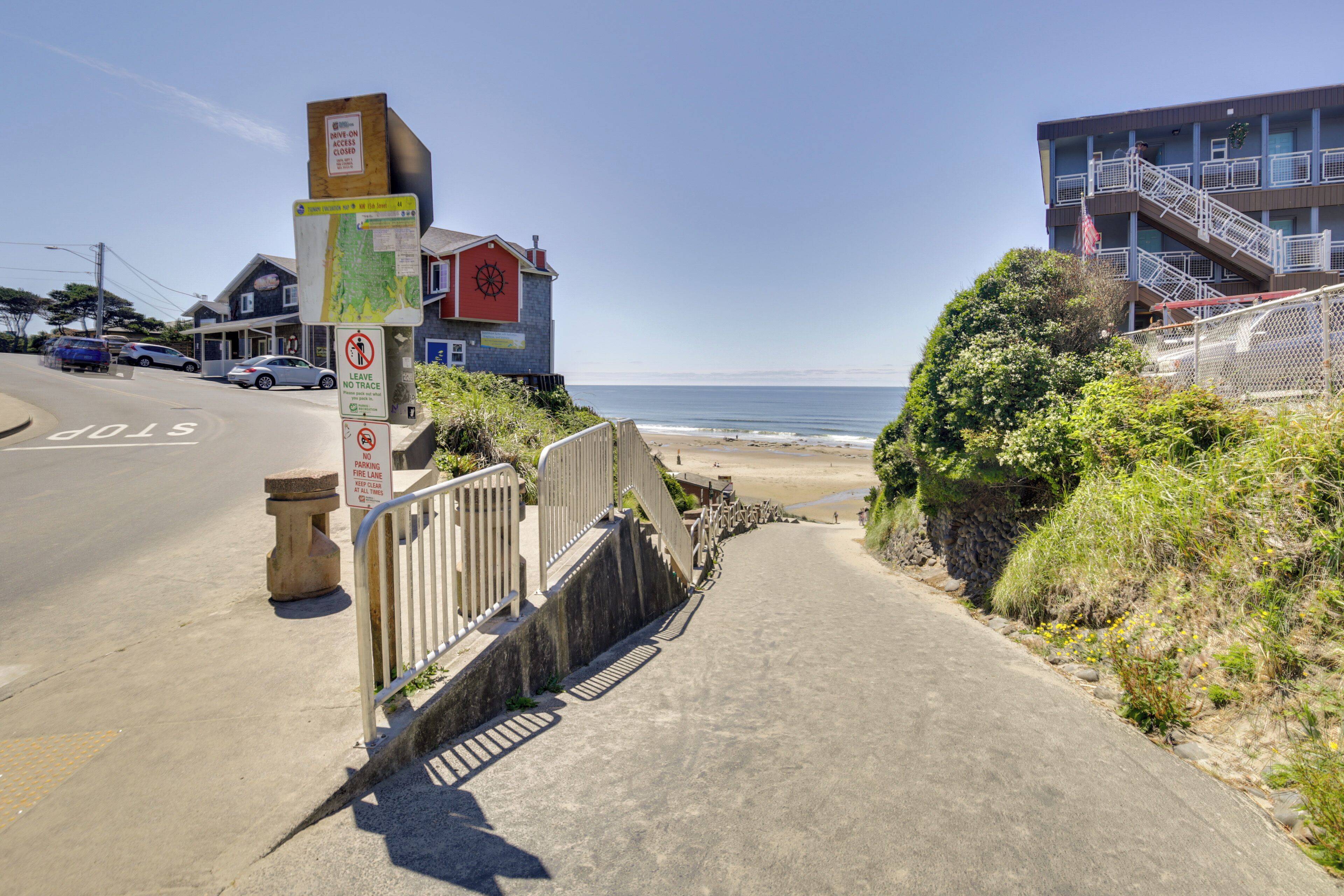 A coastal road leading to a beach with a wooden staircase and a signpost.