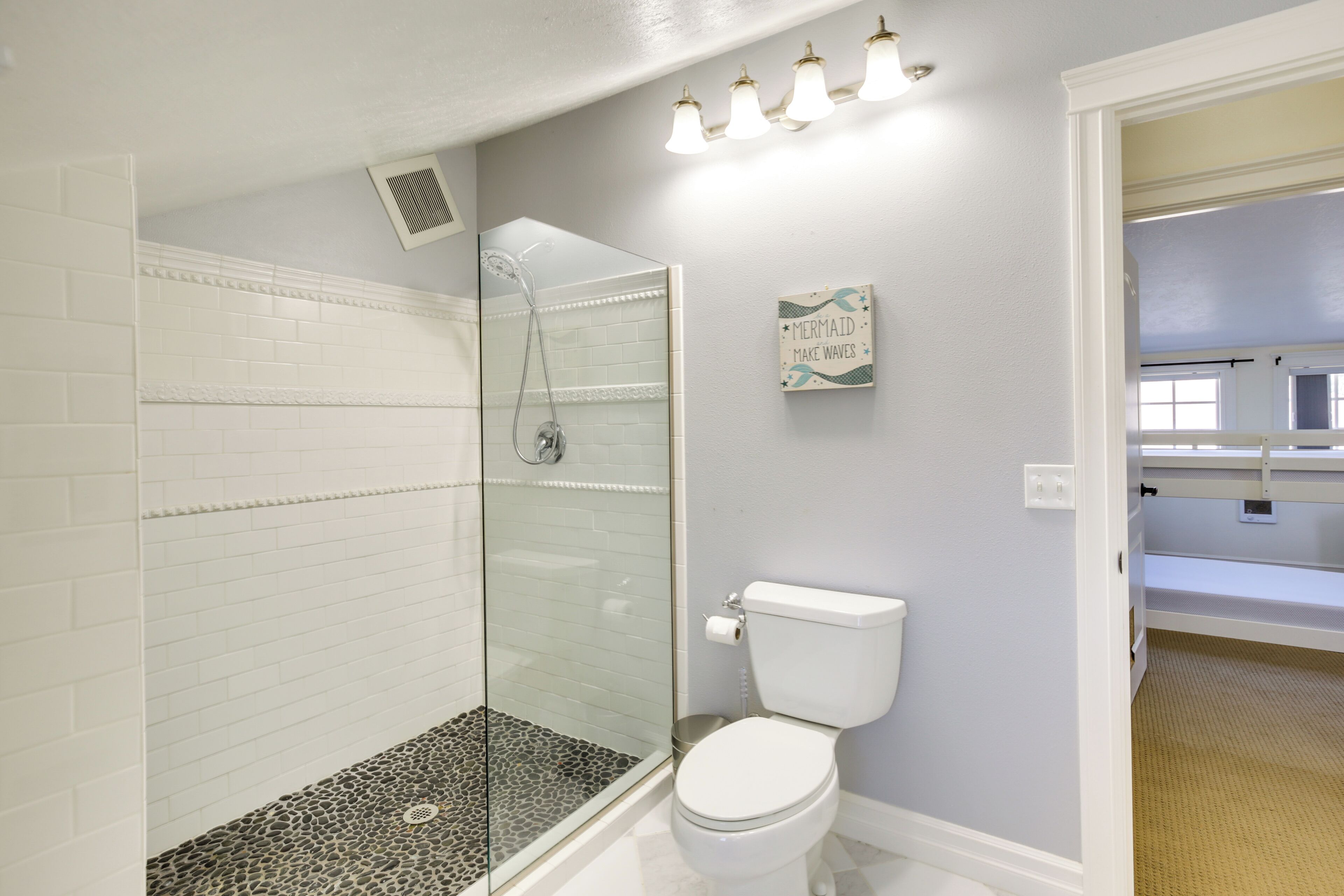 Une salle de bain avec une douche en verre, des toilettes blanches et un panneau indiquant : « Mermaid Make Waves » (en français, quelque chose comme : « La sirène fait des vagues » ou « La sirène crée l'événement »).