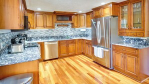 Una cocina con armarios de madera, un refrigerador de acero inoxidable, lavavajillas y encimera de granito.