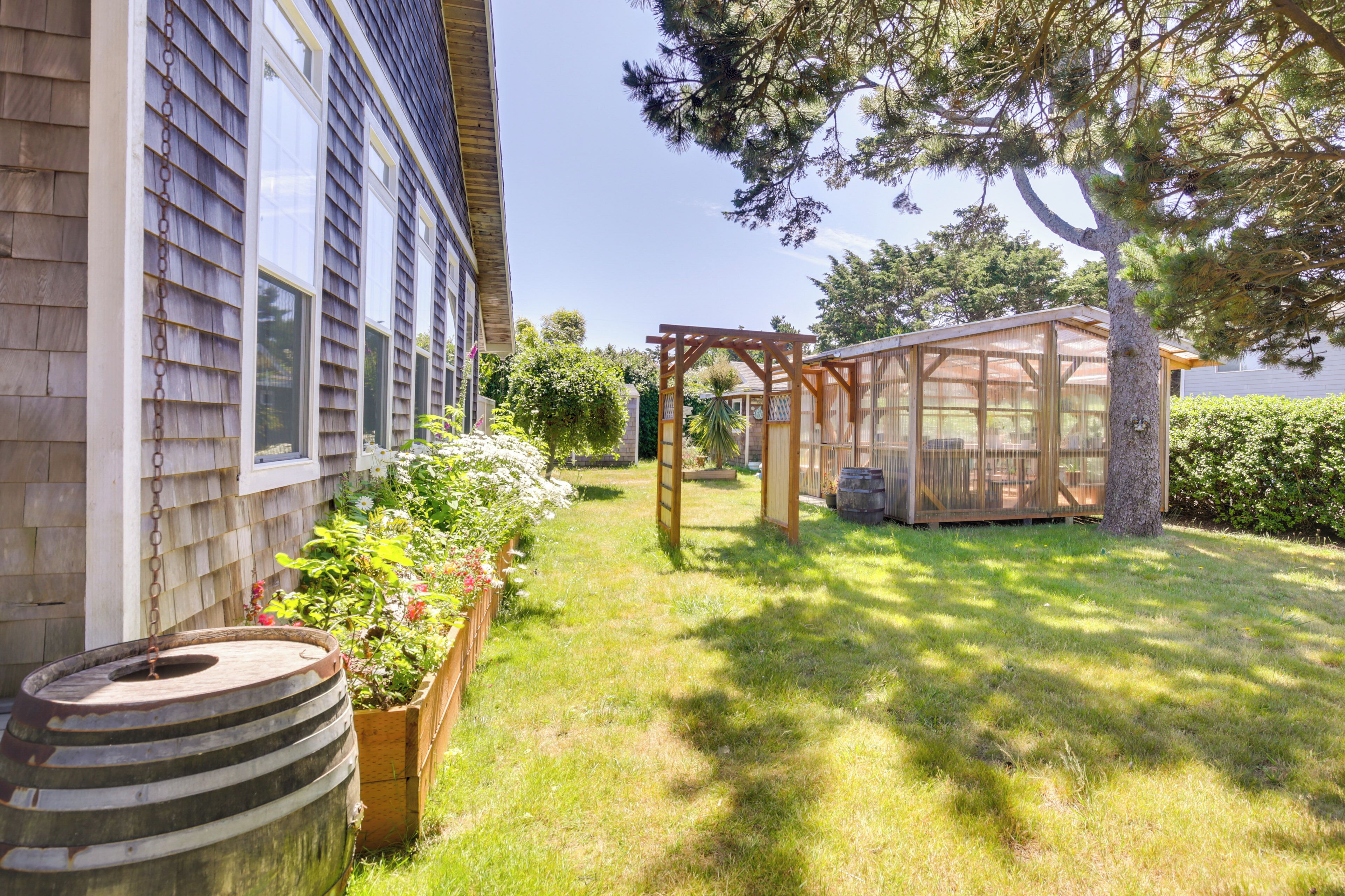 A backyard with a wooden pergola, a barrel, and a garden bed with flowers.