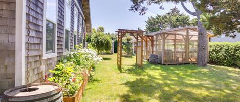 A backyard with a wooden pergola, a barrel, and a garden bed with flowers.