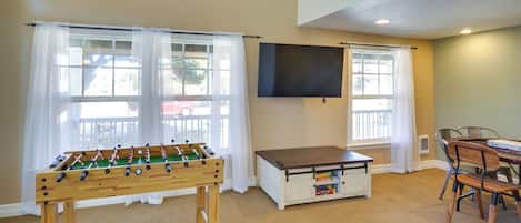 A room with a foosball table, a TV mounted on the wall, and a dining area with chairs and a table.