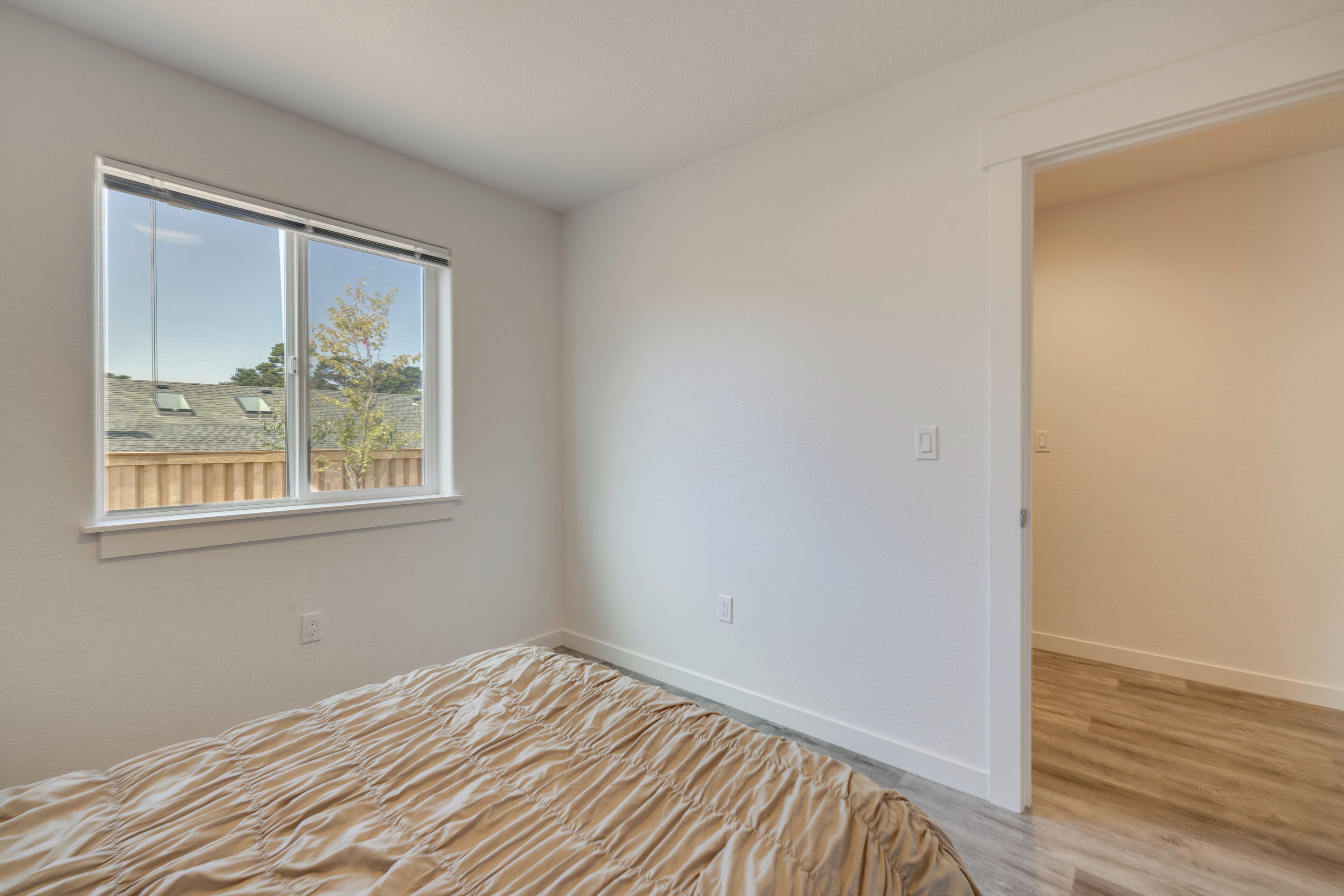 A bedroom with a large window, a bed, and a door leading to another room.