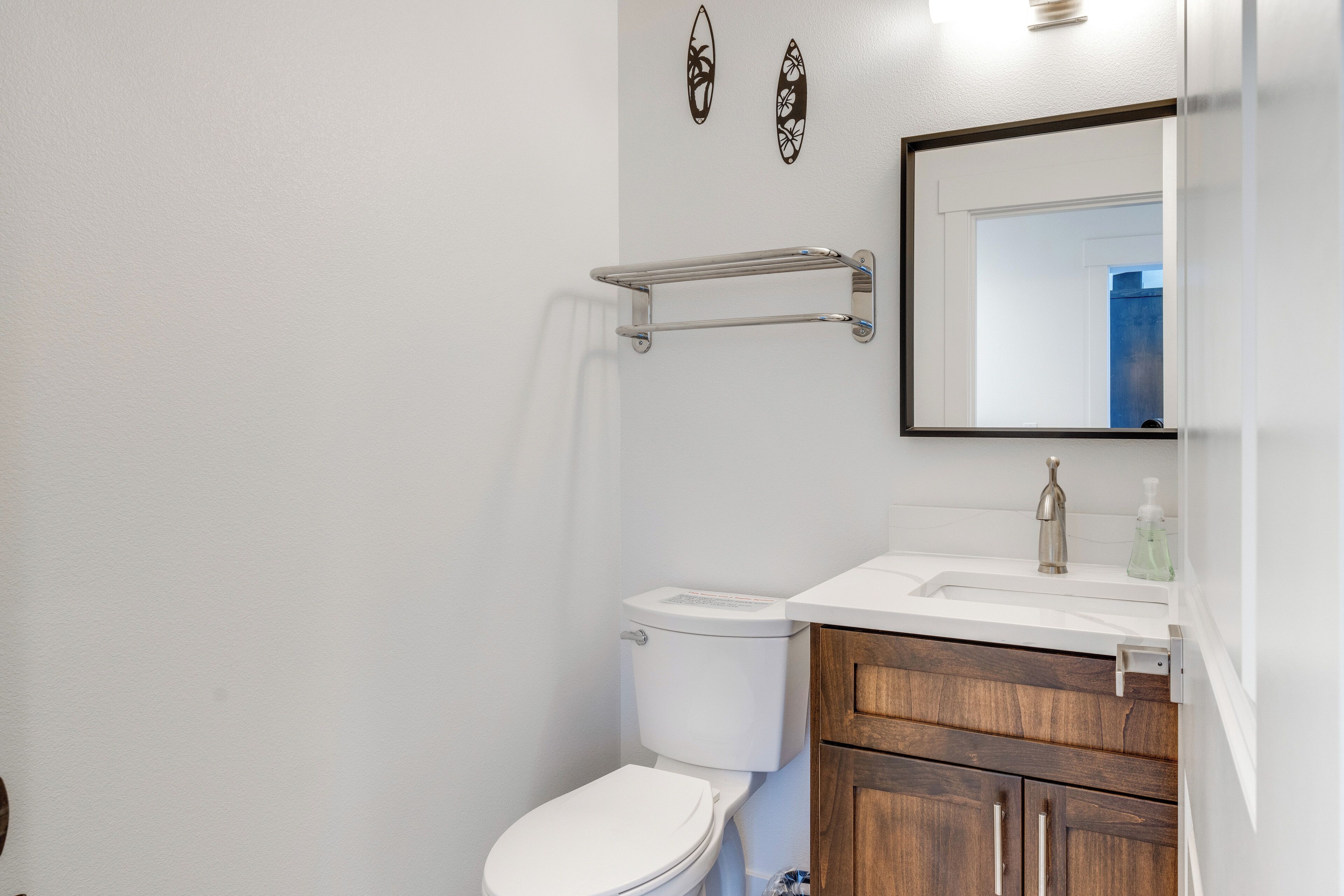 Un baño con inodoro blanco, muebles de madera, un lavamanos blanco con dispensador de jabón y un espejo sobre el lavamanos.