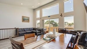 Ein geräumiges Wohnzimmer mit einem großen Esstisch aus Holz, Ledersofas und großen Fenstern mit Blick ins Freie.
