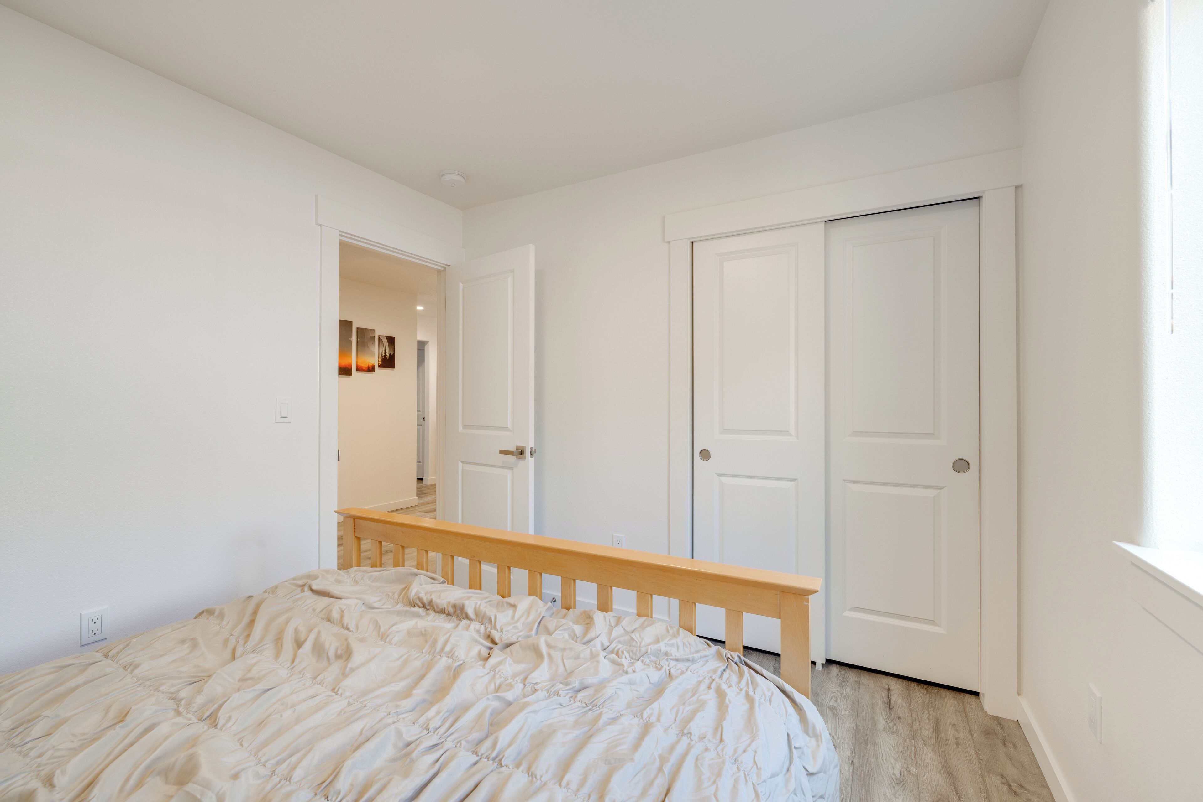 Een slaapkamer met een bed, een houten hoofdbord, witte muren en een witte deur.