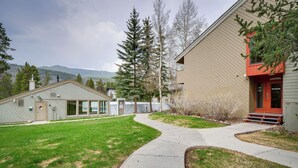 A building with a red entrance, a pathway leading to it, and a grassy area with trees. - Ski Retreat: Keystone Resort Condo w/ Heated Pool! (Keystone)
