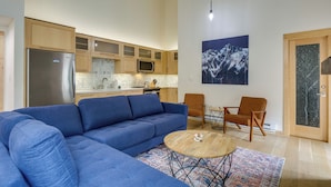 A modern living room with a blue sofa, a wooden coffee table, and two chairs. A kitchen with wooden cabinets and a refrigerator is visible in the background. - Ski Retreat: Keystone Resort Condo w/ Heated Pool! (Keystone)