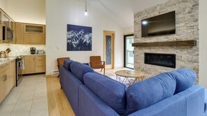 A modern living room with a blue sectional sofa, a fireplace, and a flat-screen TV mounted on a stone wall. - Ski Retreat: Keystone Resort Condo w/ Heated Pool! (Keystone)