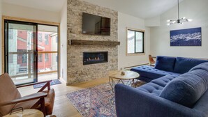 A modern living room with a stone fireplace, a blue sofa, and a television mounted on the wall. - Ski Retreat: Keystone Resort Condo w/ Heated Pool! (Keystone)