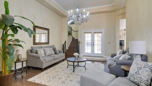 A spacious living room with a large potted plant, a chandelier, and a staircase leading to a balcony. - Luxe Yuma Home With Private Pool! (Yuma)
