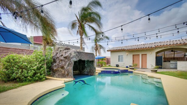 A swimming pool with a rock feature, palm trees, and string lights. - Luxe Yuma Home With Private Pool! (Yuma)