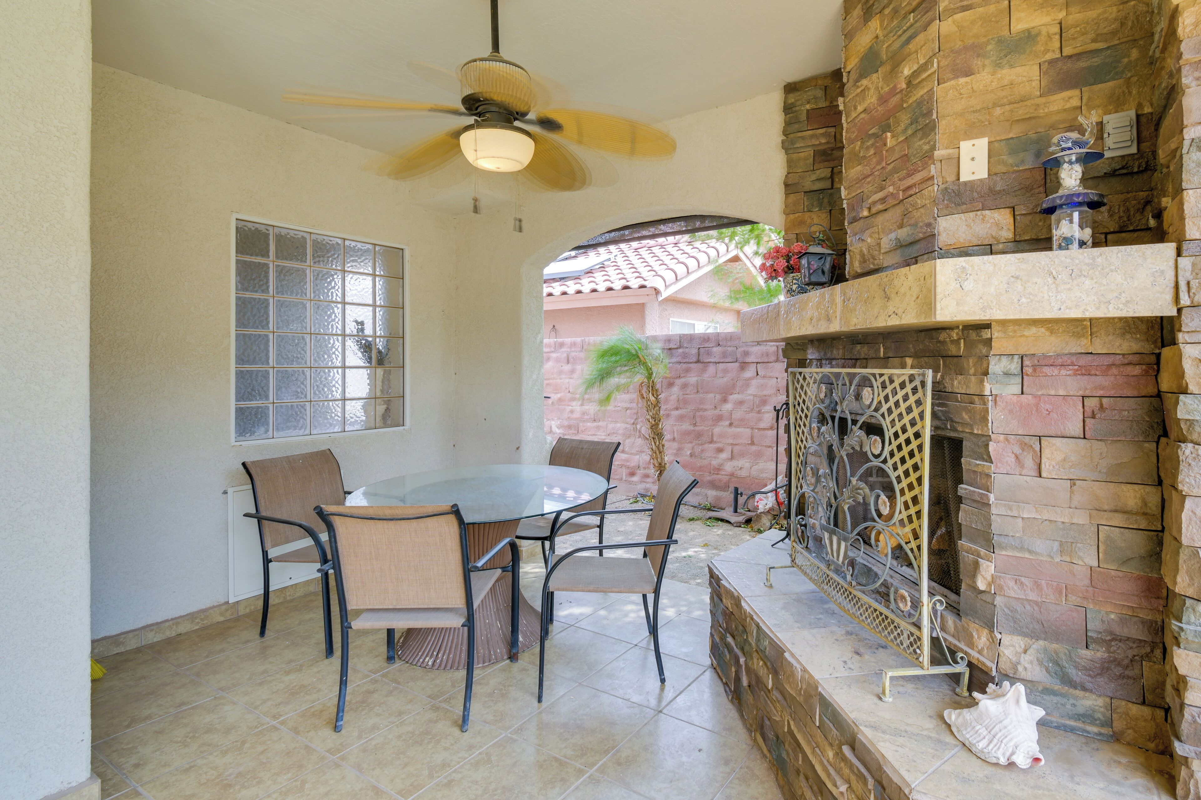A patio with a round table and chairs, a ceiling fan, and a stone fireplace.