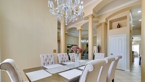 A dining area with a wooden table, six upholstered chairs, a vase with flowers, and a chandelier. - Luxe Yuma Home With Private Pool! (Yuma)