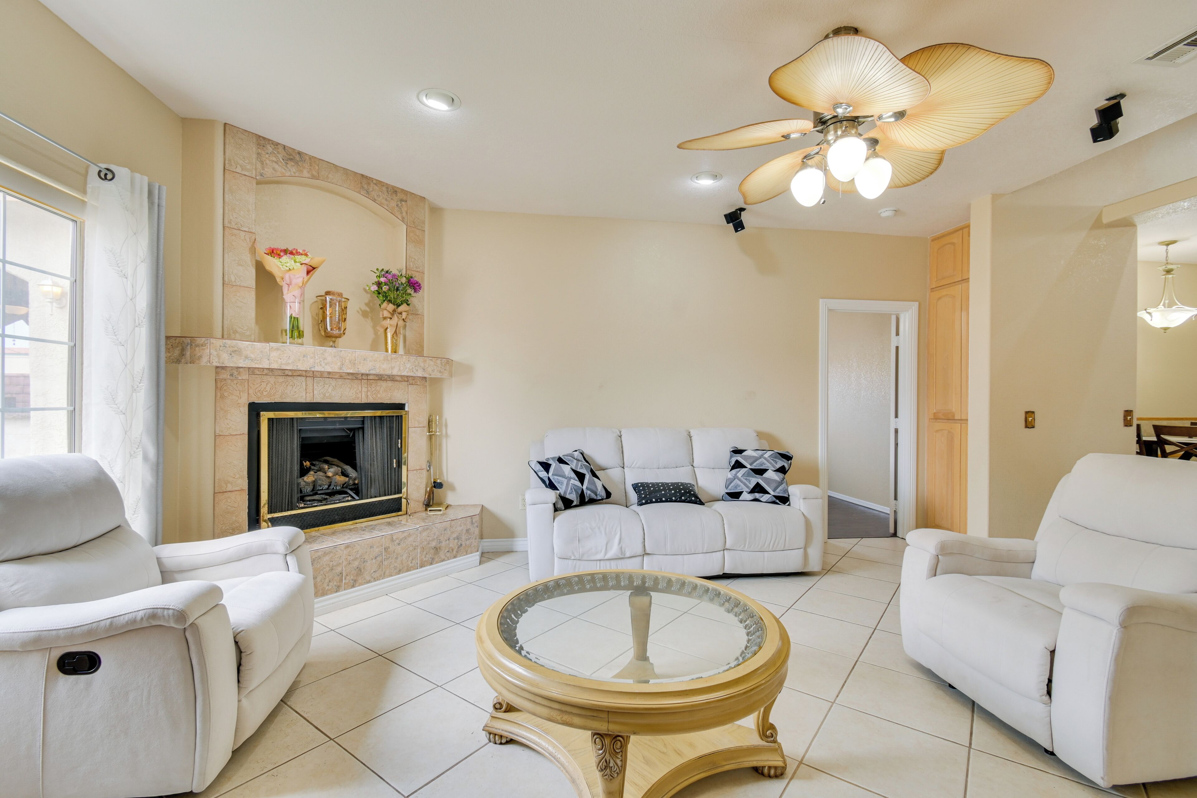 A living room with a fireplace, white sofas, a round coffee table, and a ceiling fan.