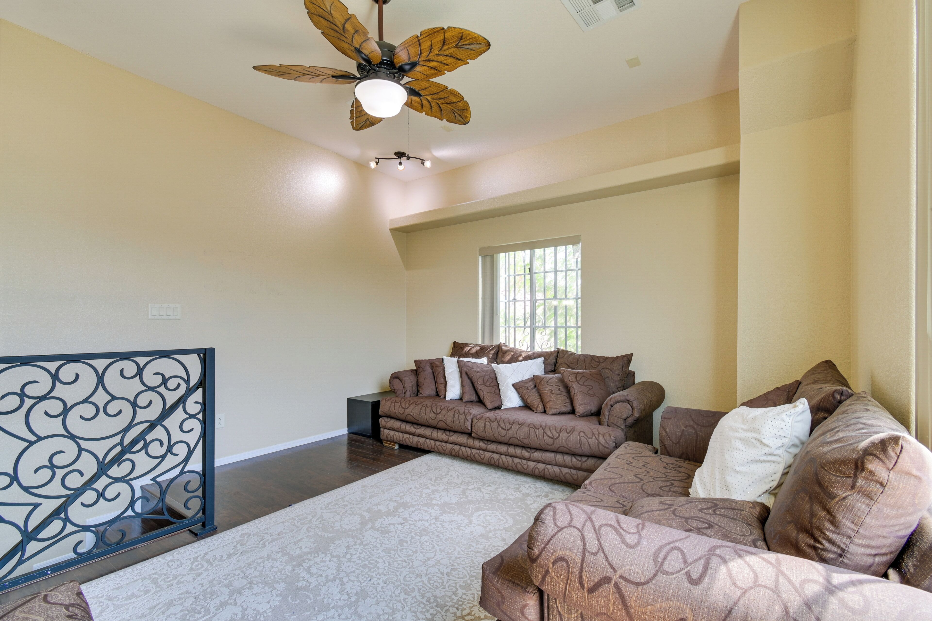 A living room with a sectional sofa, a patterned rug, a ceiling fan, and a window with blinds.