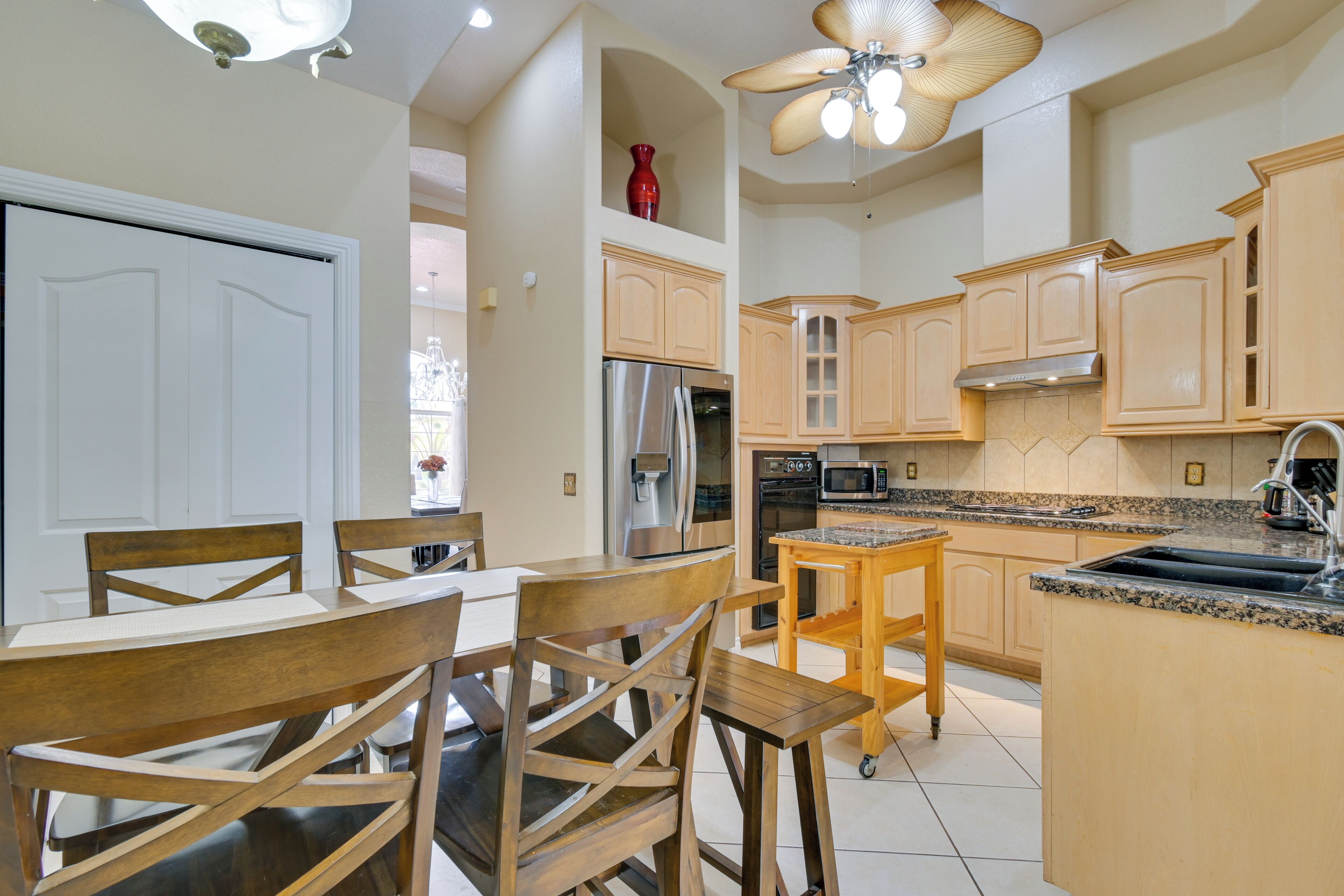 Una cucina con mobili in legno, un frigorifero in acciaio inossidabile, un forno a microonde e una ventola a soffitto.