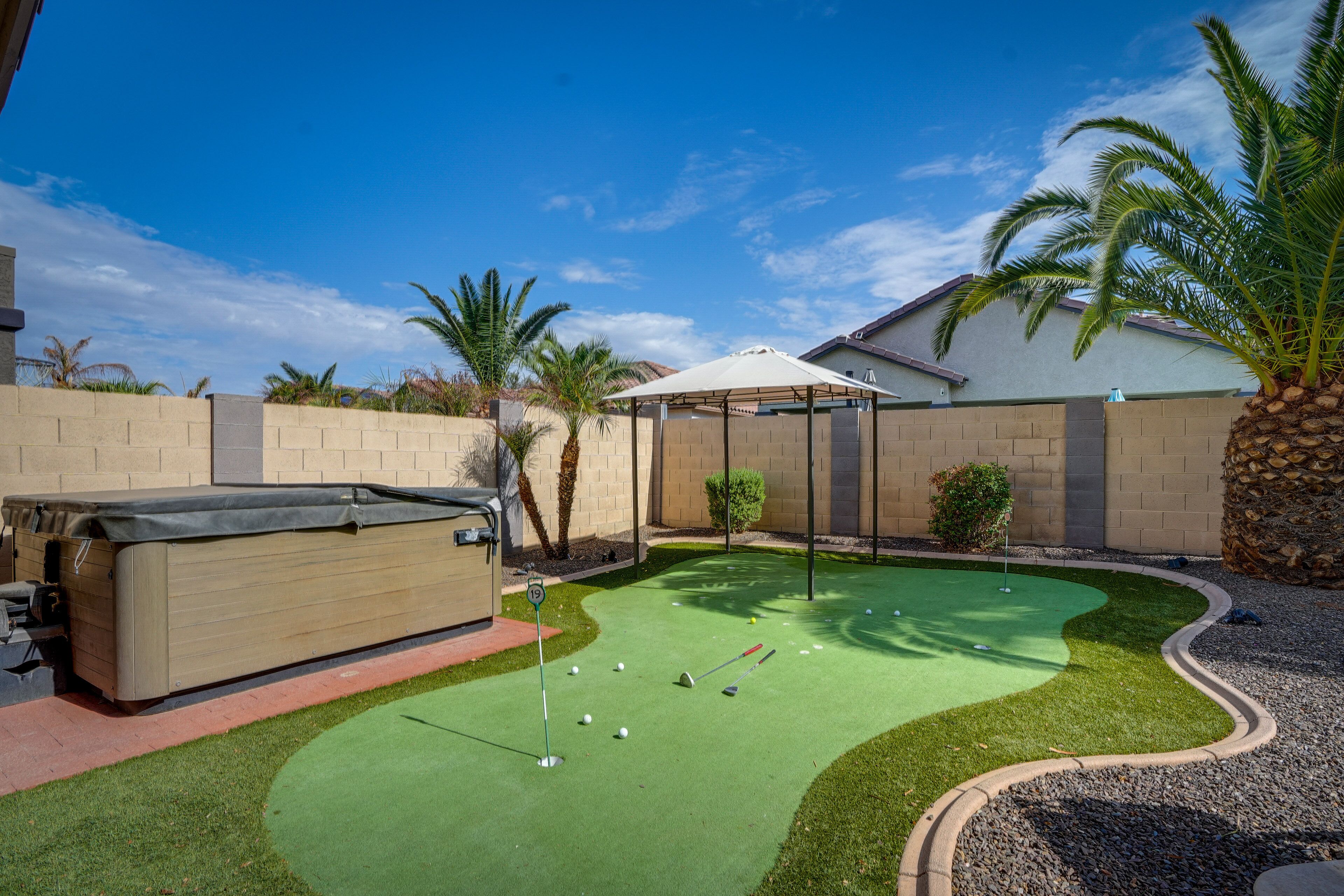 Un jardin avec un terrain d’entraînement au golf, un espace salon abrité et une piscine.