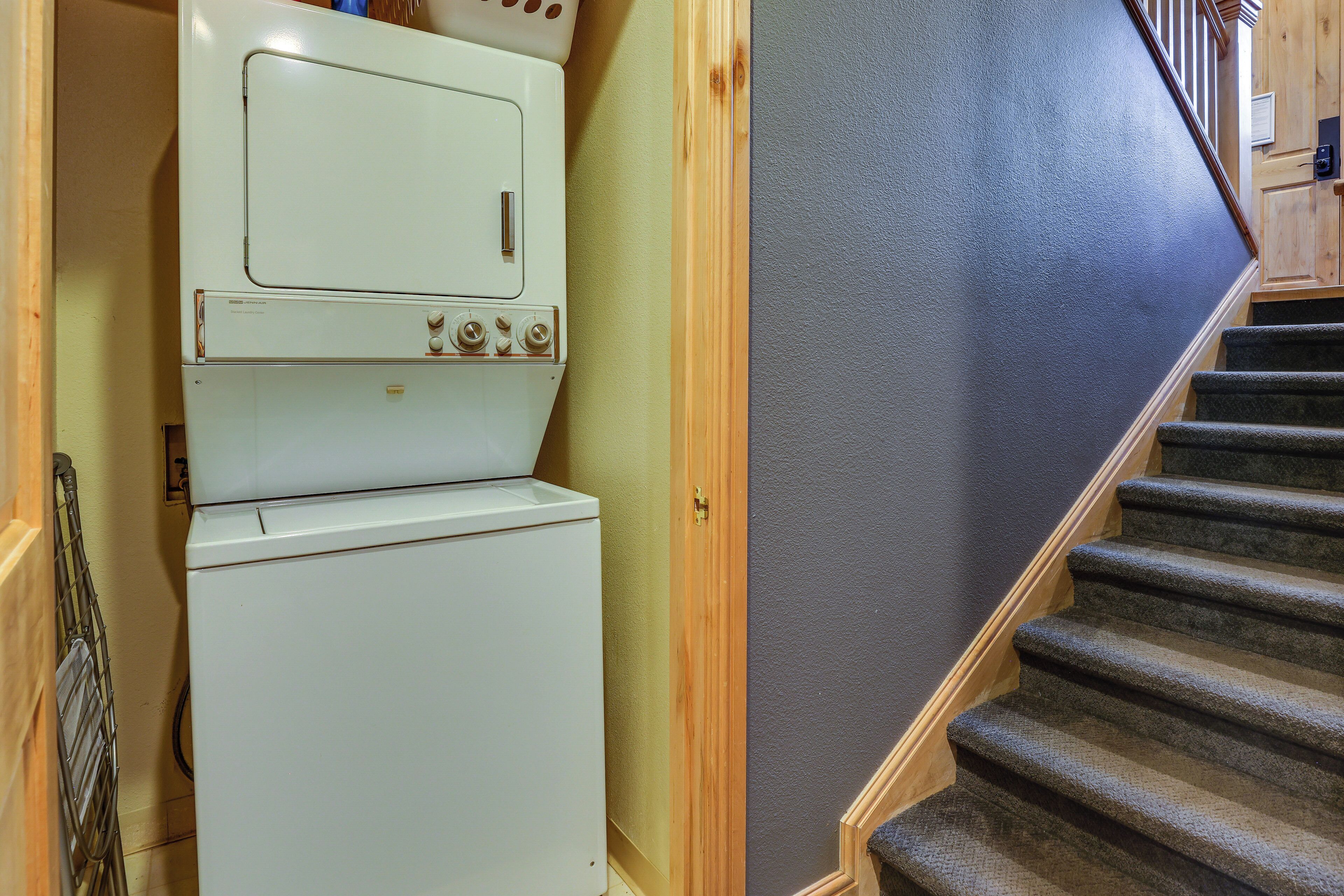A laundry room with stacked appliances and a carpeted staircase.