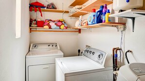A laundry room with two washing machines, shelves with cleaning supplies, and a water heater. - Pet-friendly Vacation Rental Casita in Yuma (Yuma)
