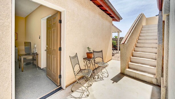A covered outdoor area with a staircase, a door leading to an interior space, and two metal chairs with a potted plant. - Pet-friendly Vacation Rental Casita in Yuma (Yuma)