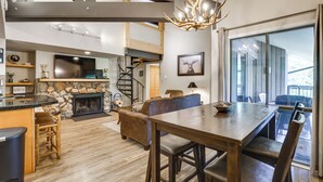 A spacious living area with a stone fireplace, a dining table with chairs, a sofa, and a staircase leading to an upper level. - Keystone Condo on Shuttle Line < 1 Mi to Resort! (Keystone)
