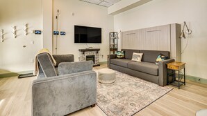 A modern living room with a grey sofa, a grey armchair, a small ottoman, a patterned rug, a flat-screen TV, a fireplace, and a wooden cabinet. - Keystone Lake Haven: Heated Pool & Ski Shuttle! (Keystone)